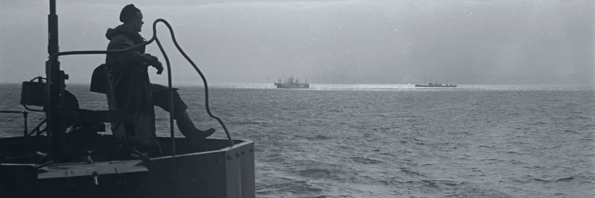 Black-and-white archive photo from the deck of a merchant tanker at sea, a seaman on watch and two ships on the horizon